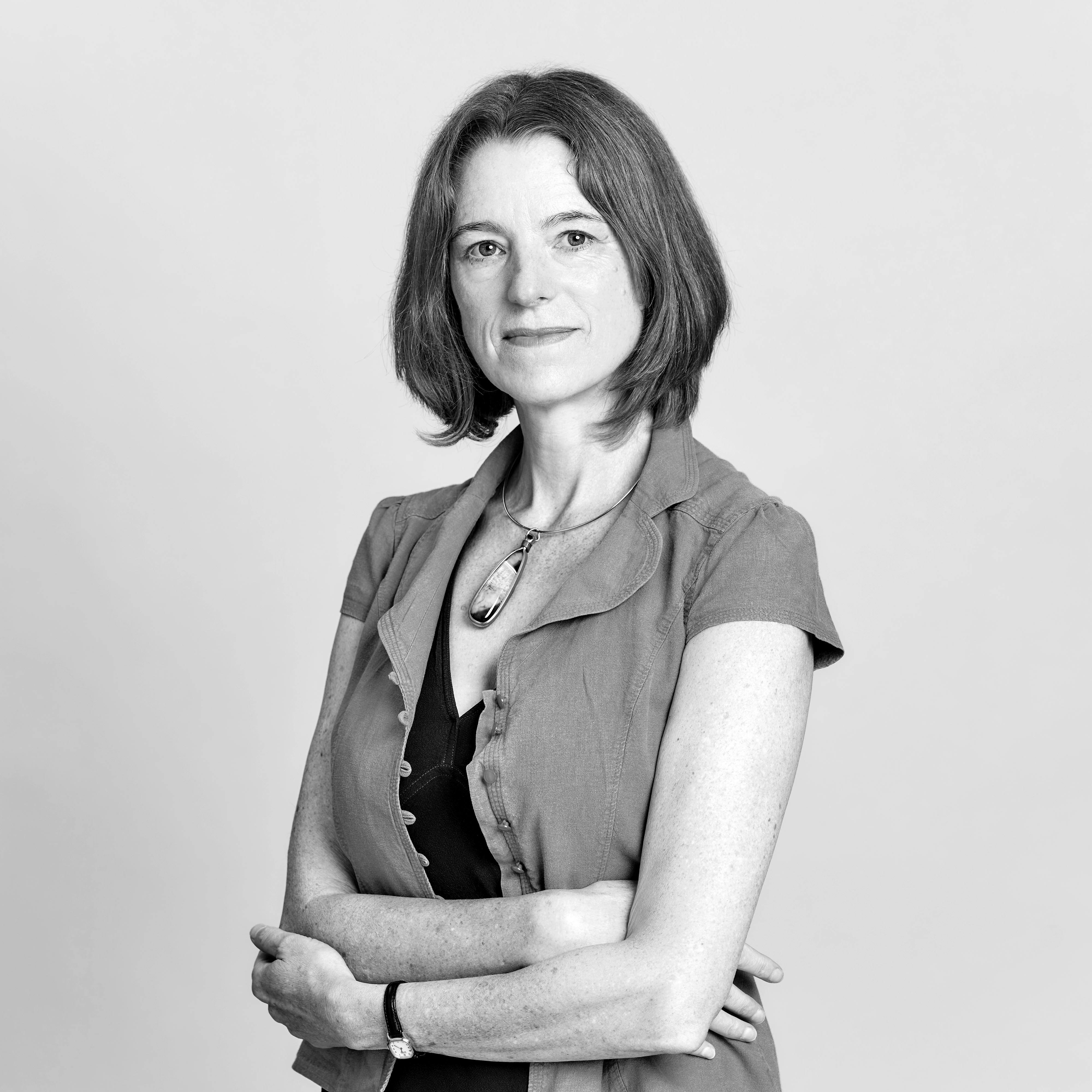 Headshot photograph of Joy MacKeith with her arms folded against a white background